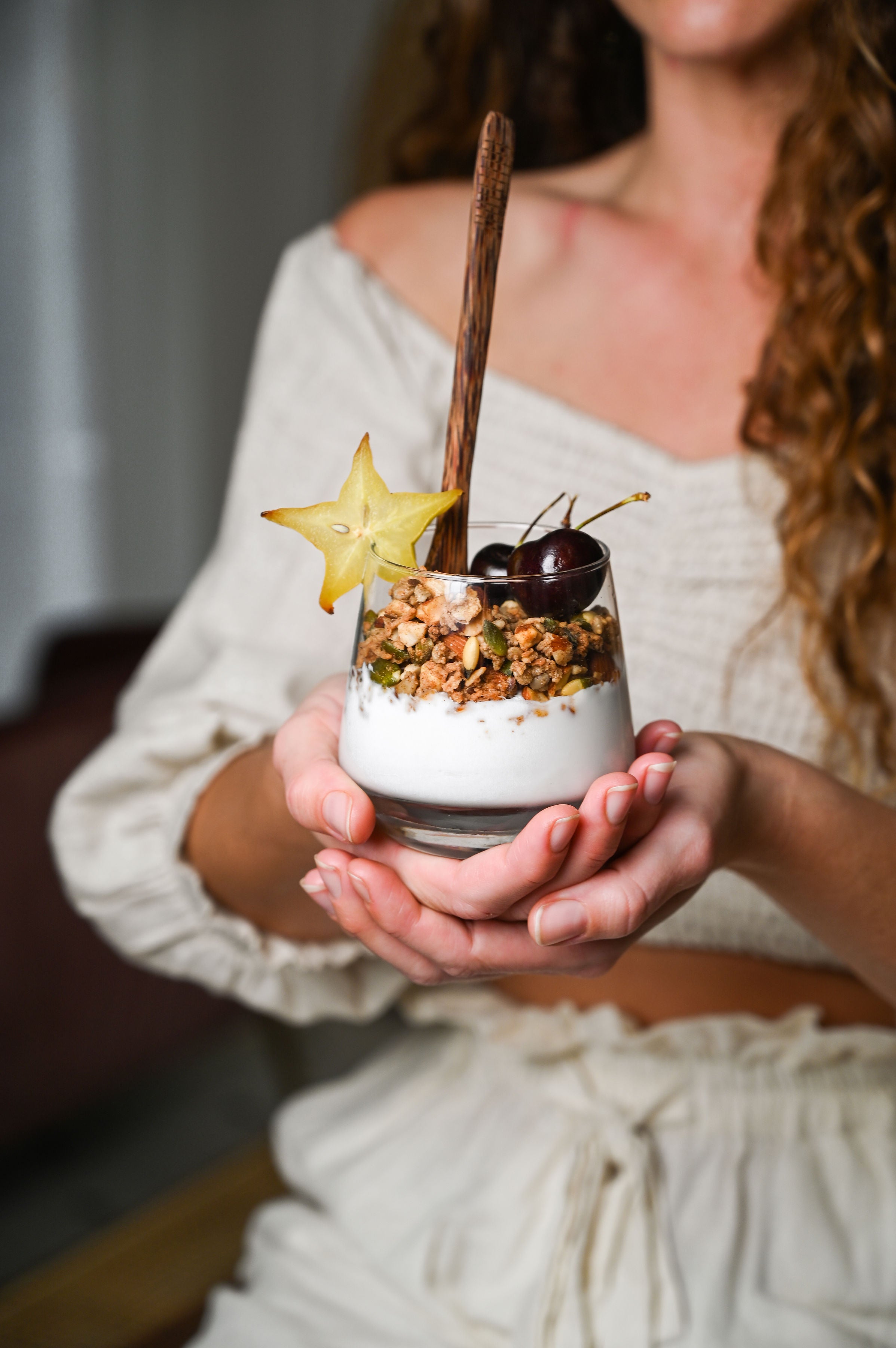 A woman holding a glass filled with vegan granola and berries